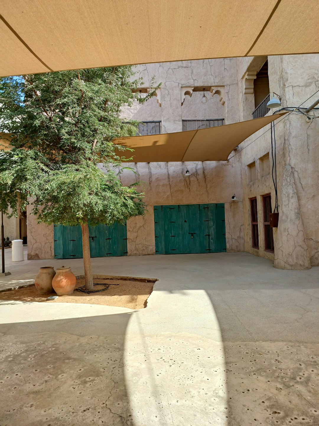 Cortile soleggiato con edifici ad arco e doppie porte verdi.